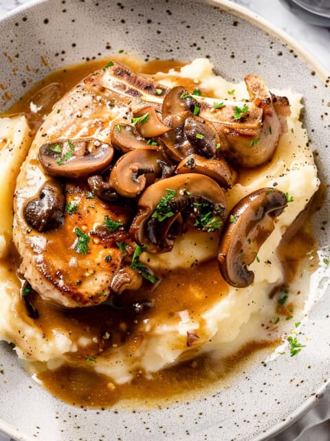 Crock pot pork chops over mashed potatoes with herbs and mushroom sauce.