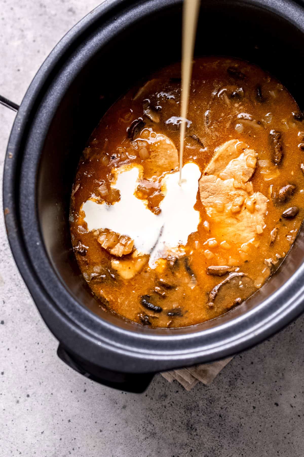 Adding cream to pork chops in a slow cooker.