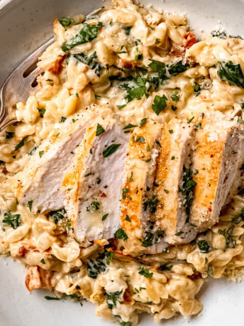 Tuscan chicken orzo in a white bowl on a blue table.