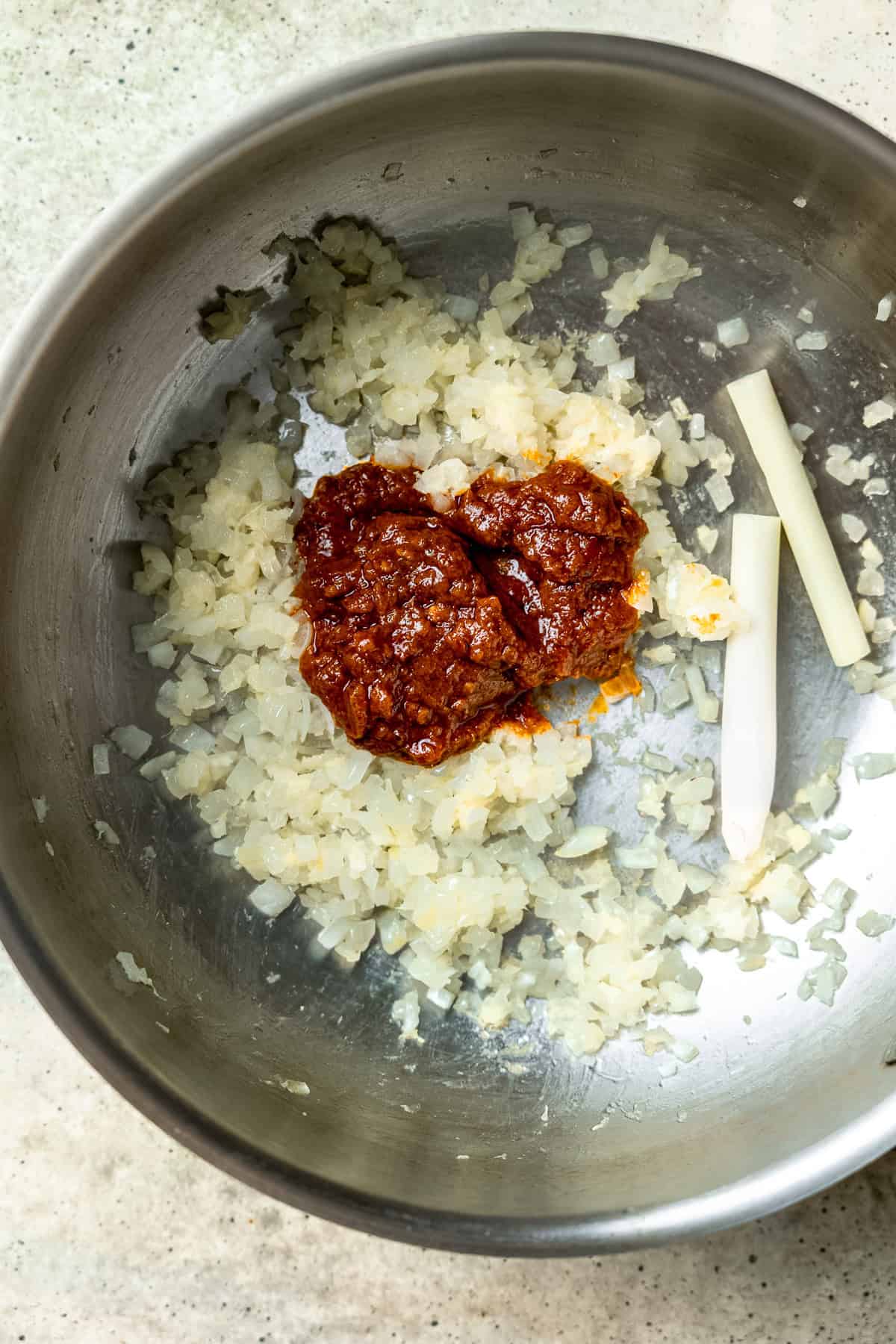 Red curry paste being added to the pot with ginger and lemongrass.